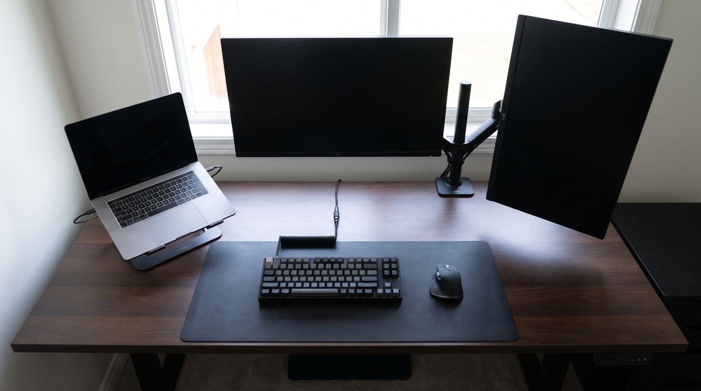 Top-down view of a programmer's dual monitor desk with the main monitor centered and a second monitor rotated to portrait on the right, cables routed through the arm